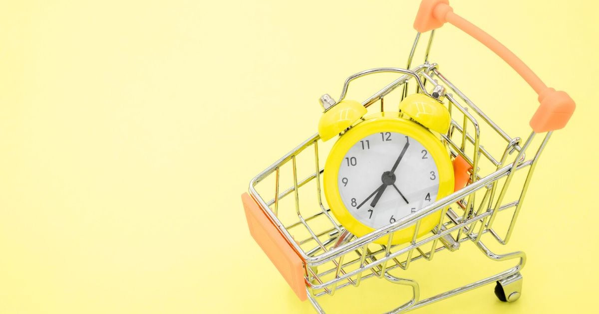 Orange shopping trolley with a yellow alarm clock inside, on a yellow background