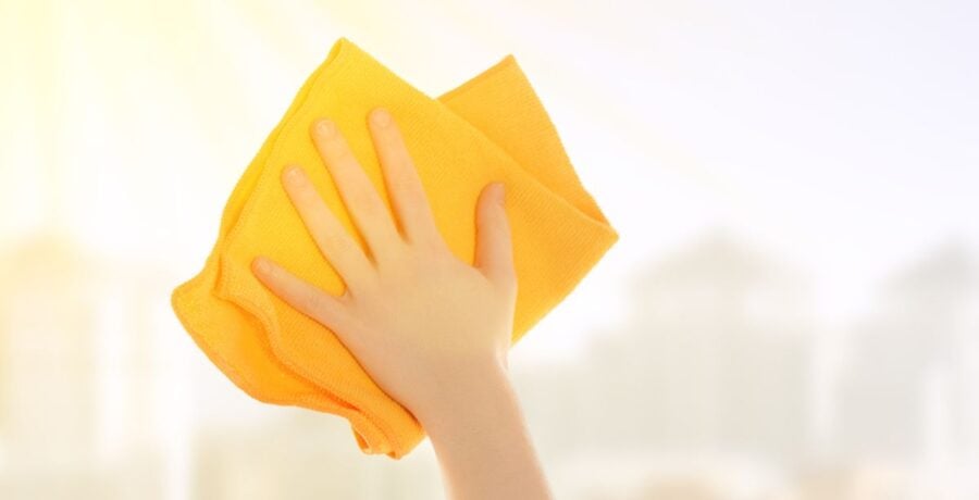 Hand with a yellow clothe cleaning a window